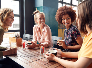 Four Young Female Friends Meeting Sit At Table In Coffee Shop And Talk