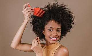 African American woman detangling her natural hair using a wide toothed comb as she is smiling