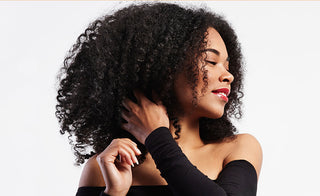 black woman looking to the side as she is touching her natural curly hair and she is smiling with her eyes closed