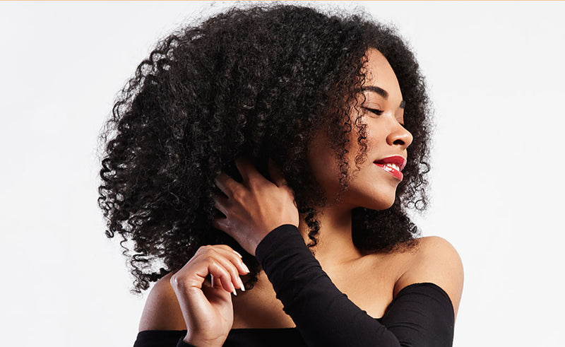 black woman looking to the side as she is touching her natural curly hair and she is smiling with her eyes closed
