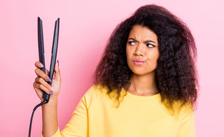 Close up photo beautiful lady with natural curly hair looking at ceramic hot tool equipment curler not sure about using dangerous tool because of potential damage. isolated beige background