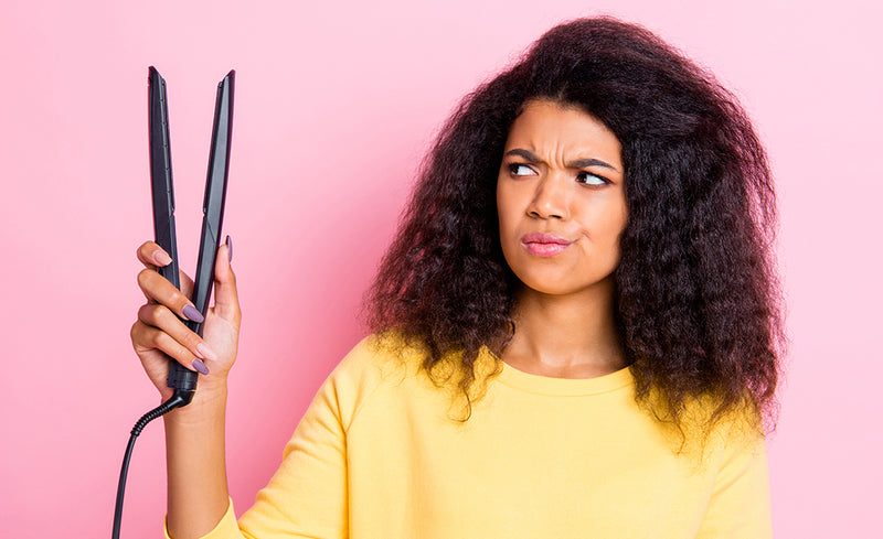 Close up photo beautiful lady with natural curly hair looking at ceramic hot tool equipment curler not sure about using dangerous tool because of potential damage. isolated beige background