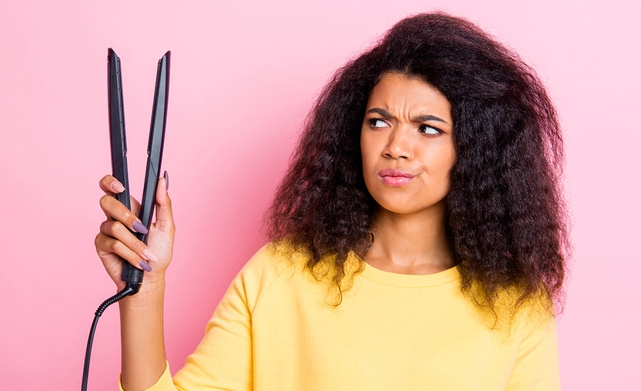 Close up photo beautiful lady with natural curly hair looking at ceramic hot tool equipment curler not sure about using dangerous tool because of potential damage. isolated beige background