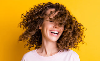 woman with short curly hair smiling in front of a yellow background