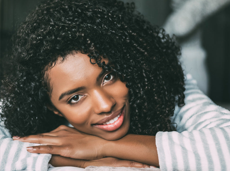 Close up of Black woman with 3b curly hair smiling and lying on bed looking at the camera
