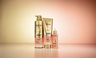 Bottles of Pantene Abundant & Strong shampoo, conditioner and serum, clinically proven for effective female hair loss treatment, in front of a gold and pink background. 