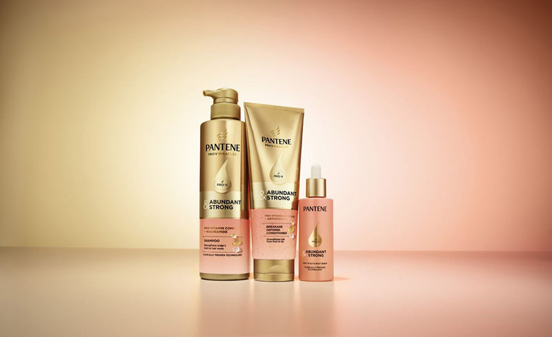 Bottles of Pantene Abundant & Strong shampoo, conditioner and serum, clinically proven for effective female hair loss treatment, in front of a gold and pink background. 